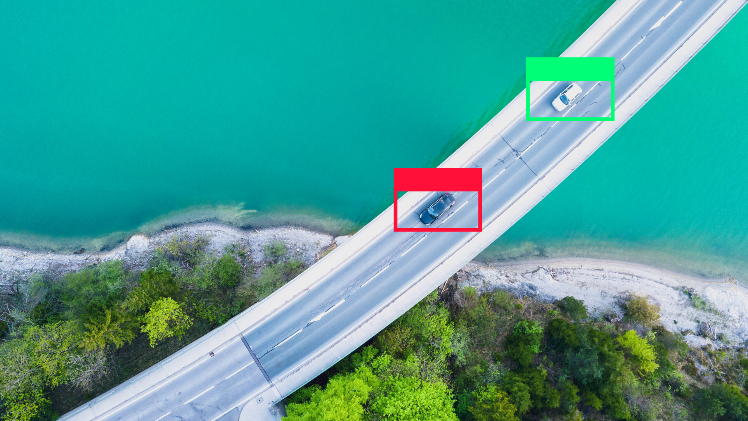 Aerial view of two cars traveling in opposite directions on a highway beside a shoreline.