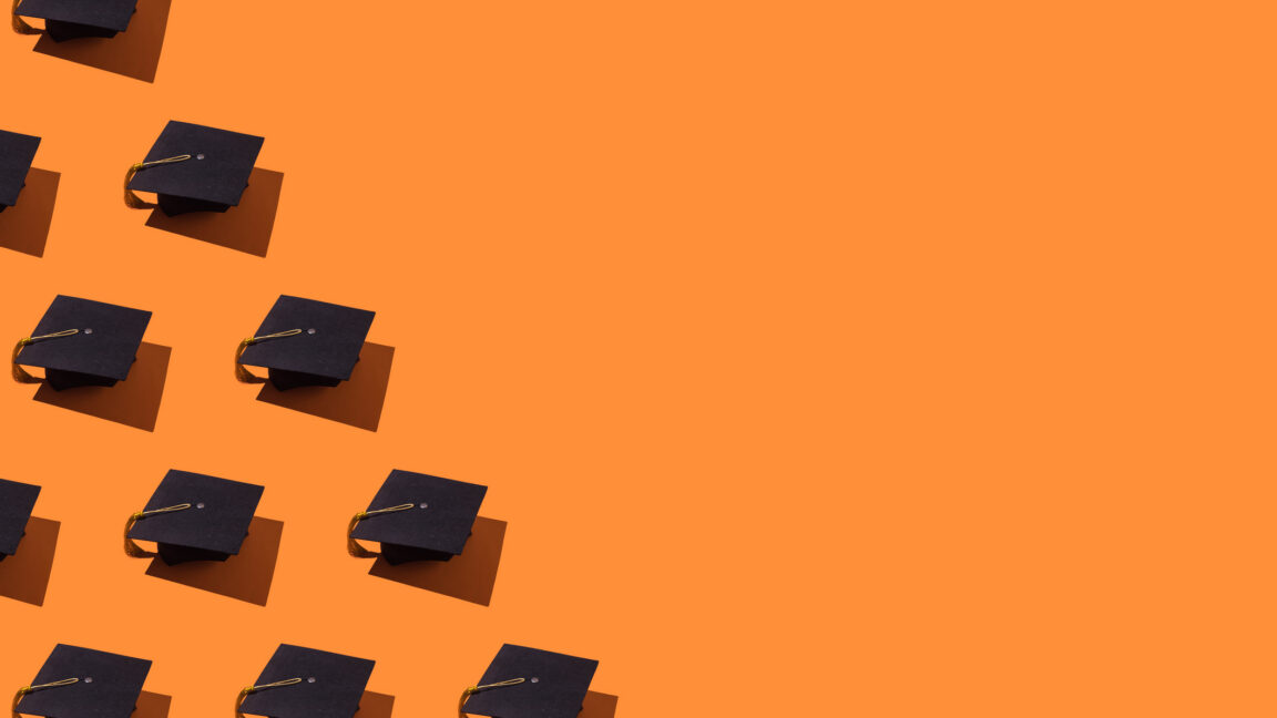 Black graduation caps with gold tassels cast shadows across a bright orange surface.