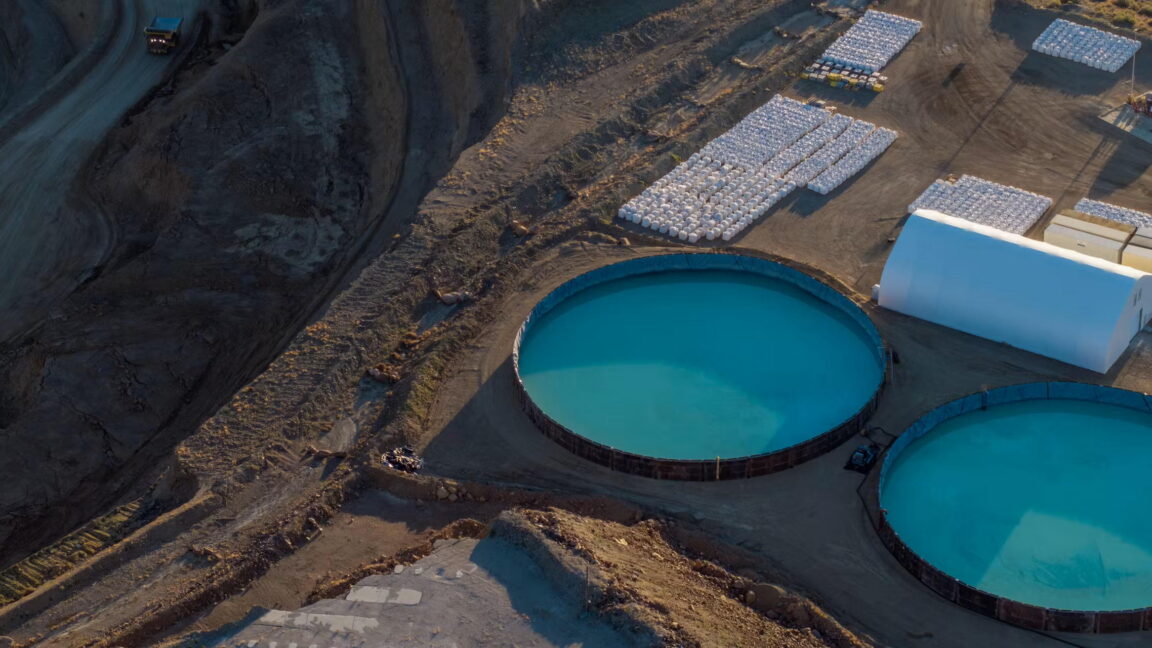 Aerial view of large circular blue tanks and rectangular industrial structures on barren ground.