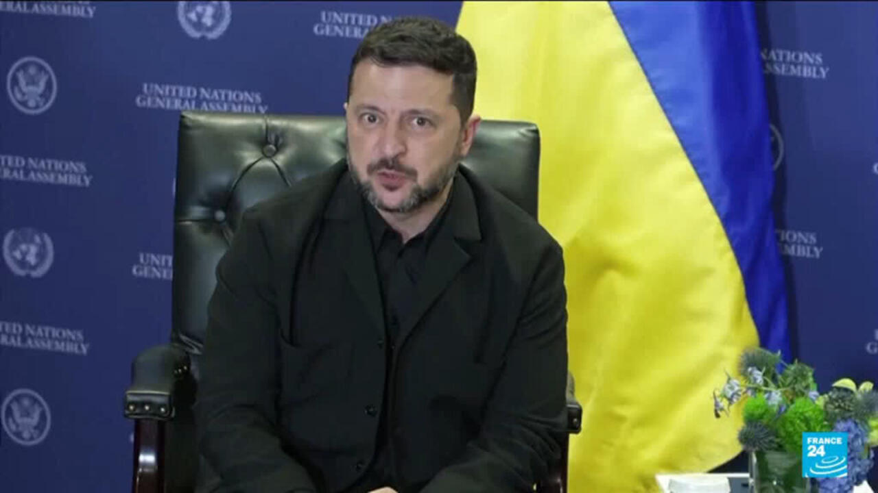 A man in a dark suit sits before a Ukrainian flag and a United Nations General Assembly backdrop.