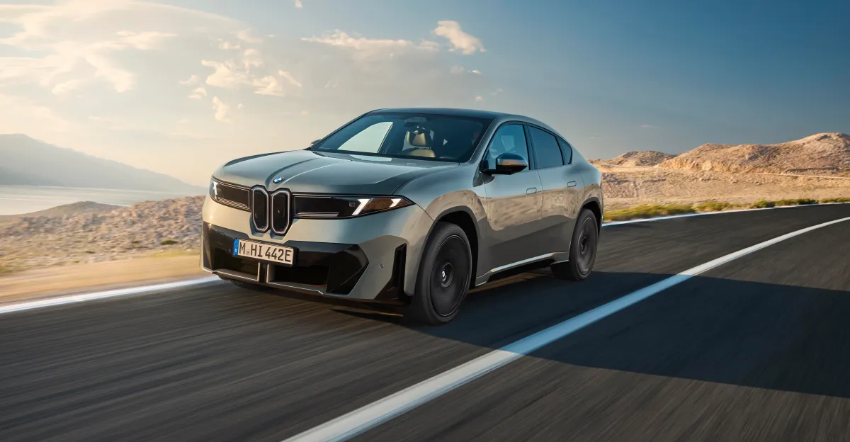Silver BMW electric SUV driving on a paved road through a dry, mountainous landscape.