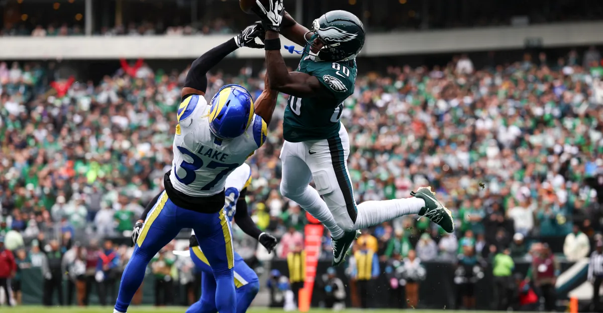 An Eagles player leaps to catch a football over a Rams defender during a game.