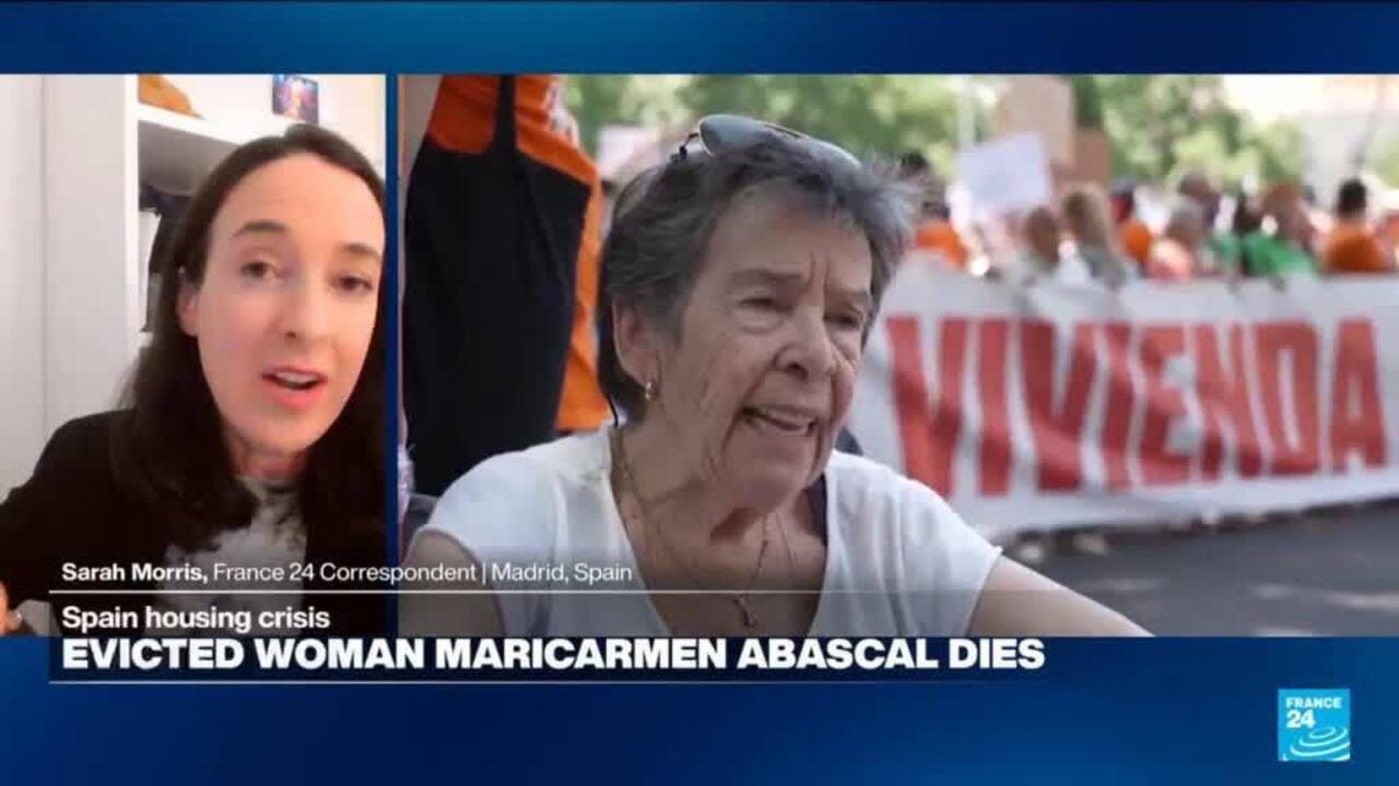 News broadcast shows a woman speaking beside an elderly woman seated before a housing protest banner.