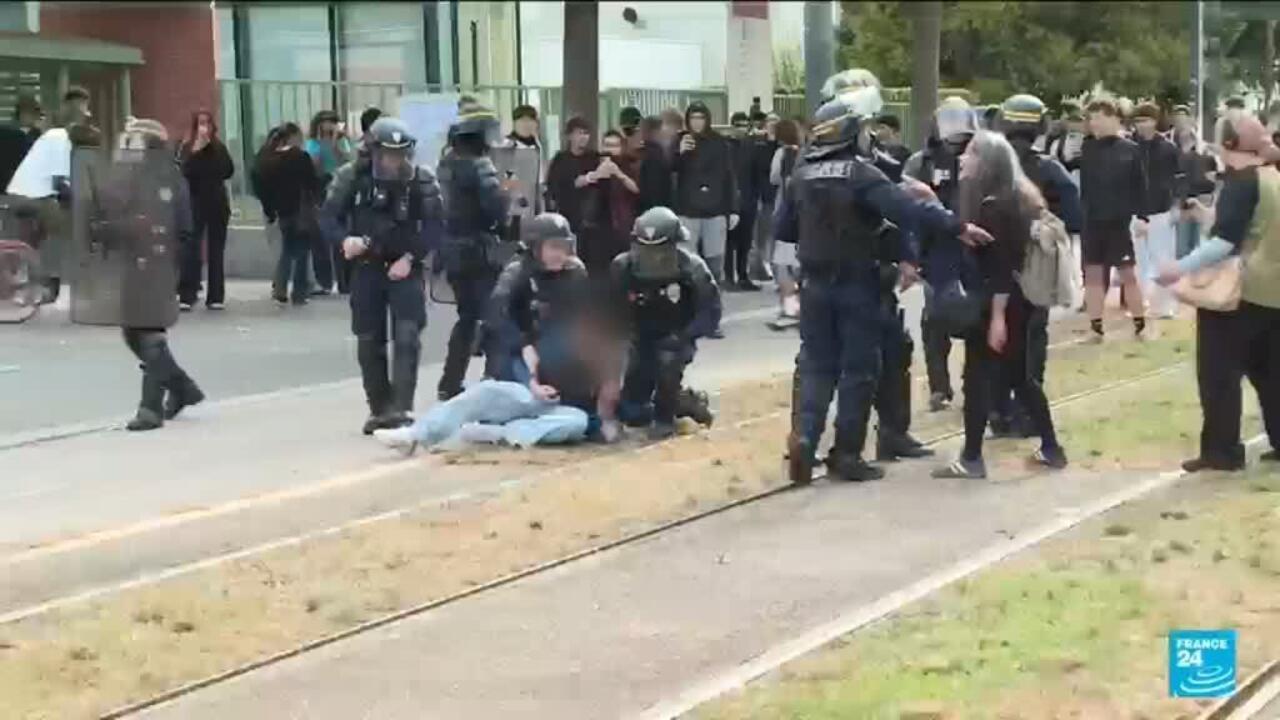 Police officers restrain a person on the ground as bystanders gather beside tram tracks.