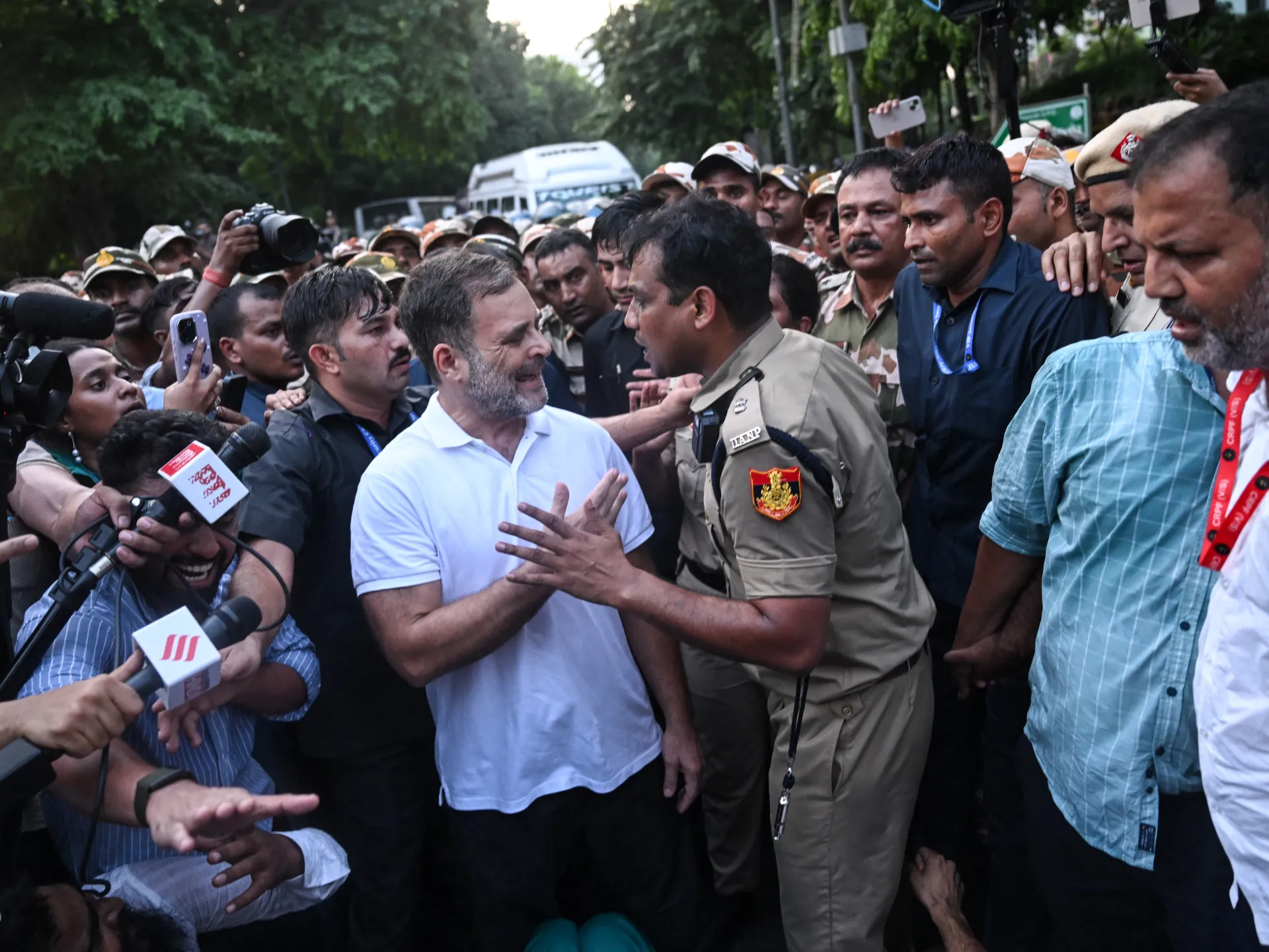 Rahul Gandhi speaks with a uniformed officer as journalists and security personnel crowd around them.