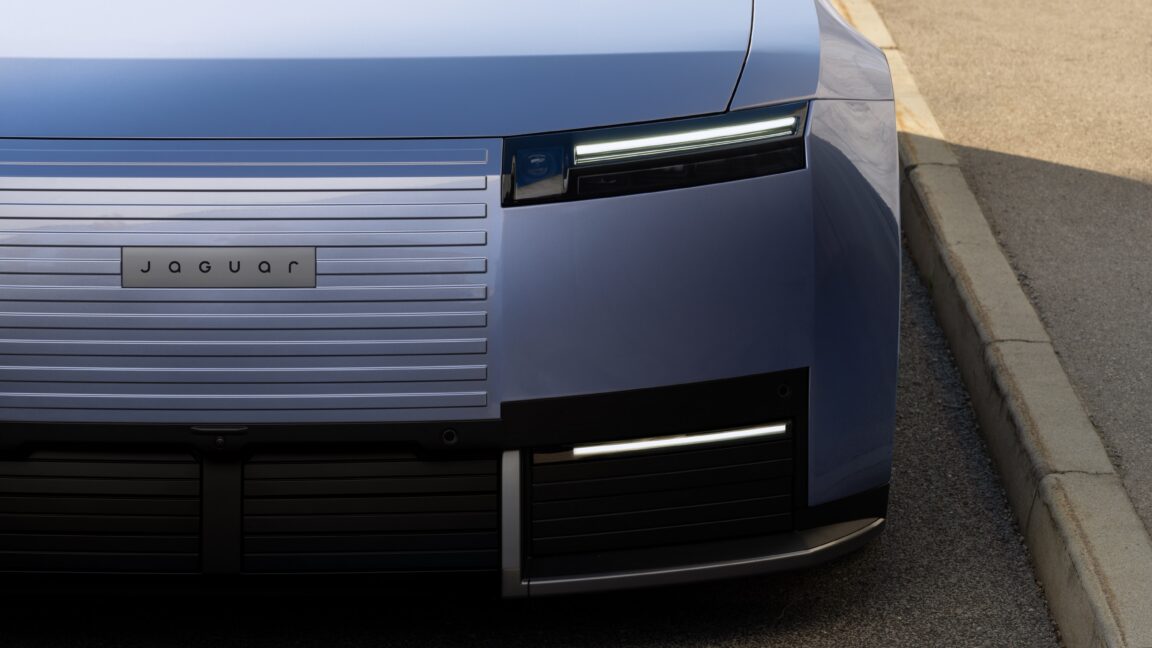 Close-up of a blue Jaguar car’s front grille and headlights beside a paved curb.