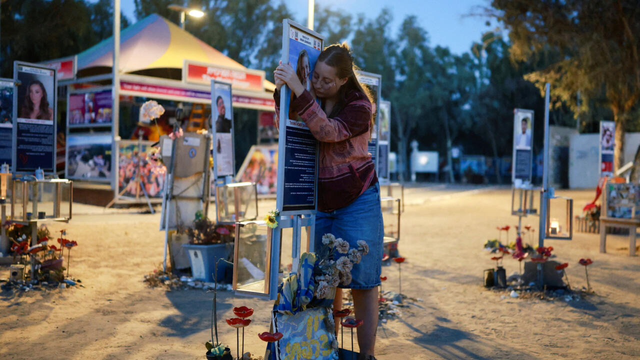 A woman embraces a memorial display amid flowers and photographs at dusk.