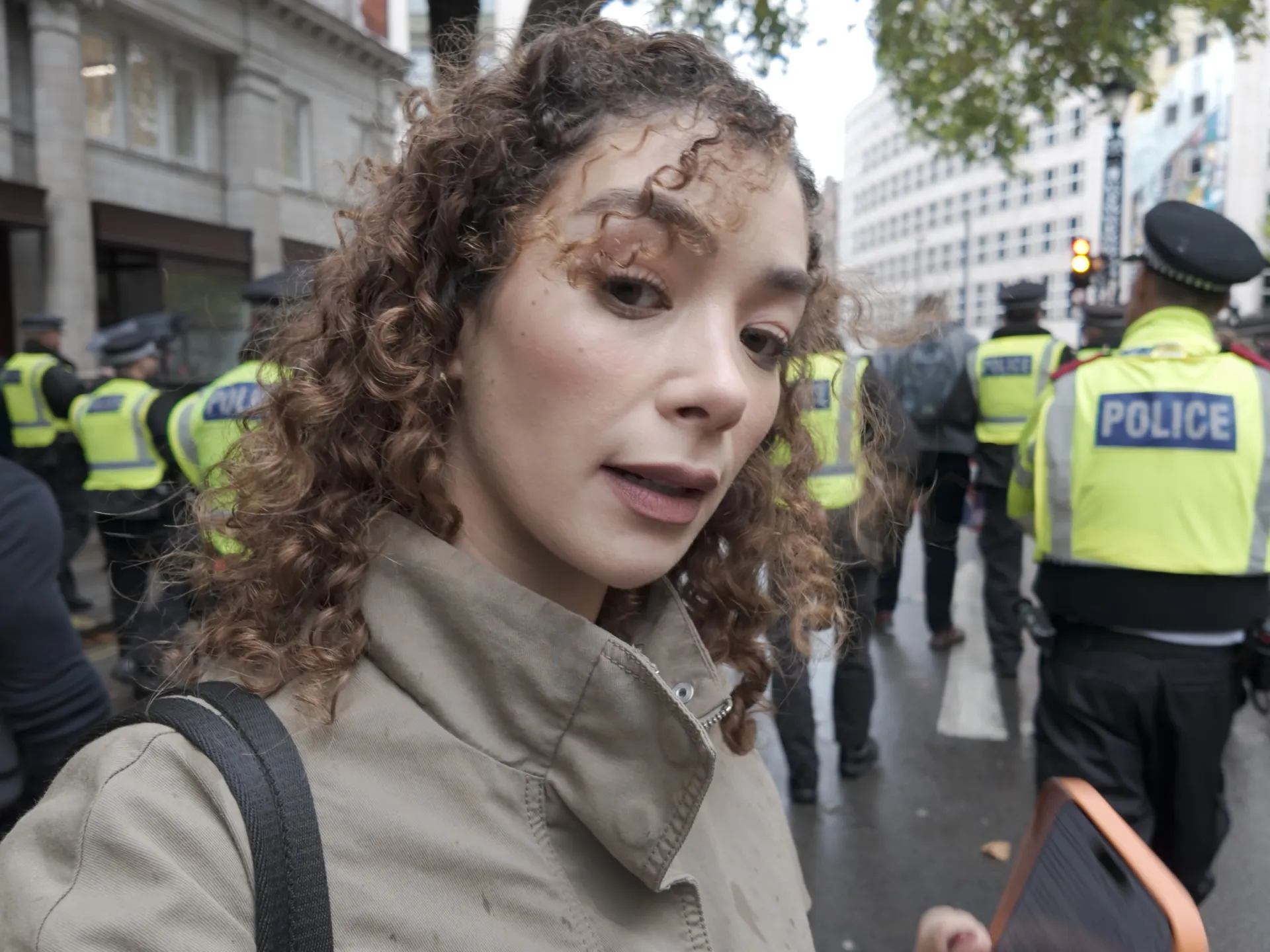 A woman holds a phone near police officers in high-visibility jackets on a city street.