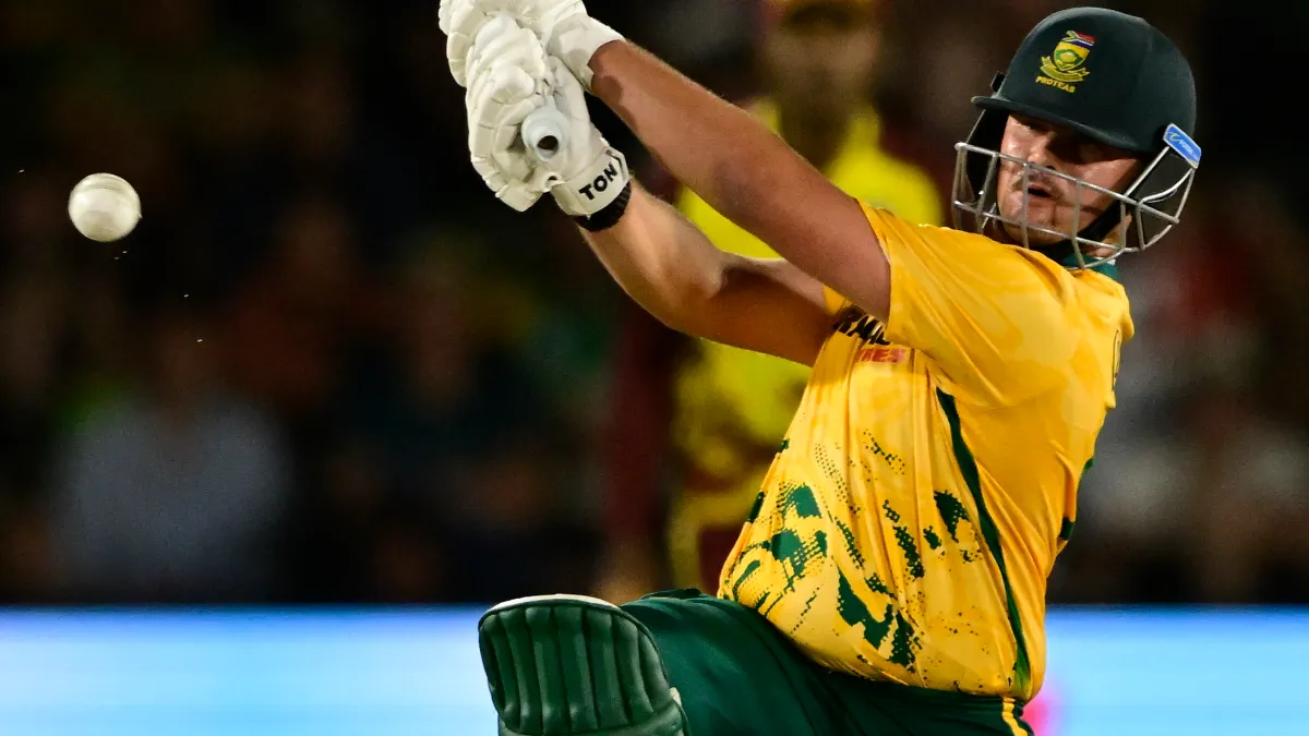 A South African batter in a yellow jersey swings at a ball during a cricket match.