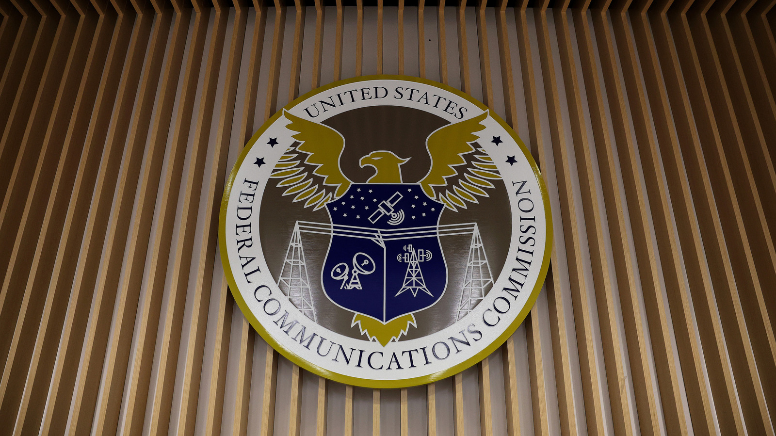 Federal Communications Commission seal mounted on a wall of vertical wooden slats.