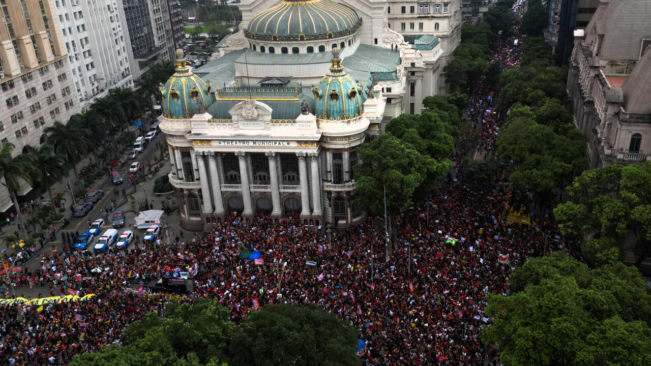 Aerial view of a large crowd gathered around an ornate domed theater in a city center.
