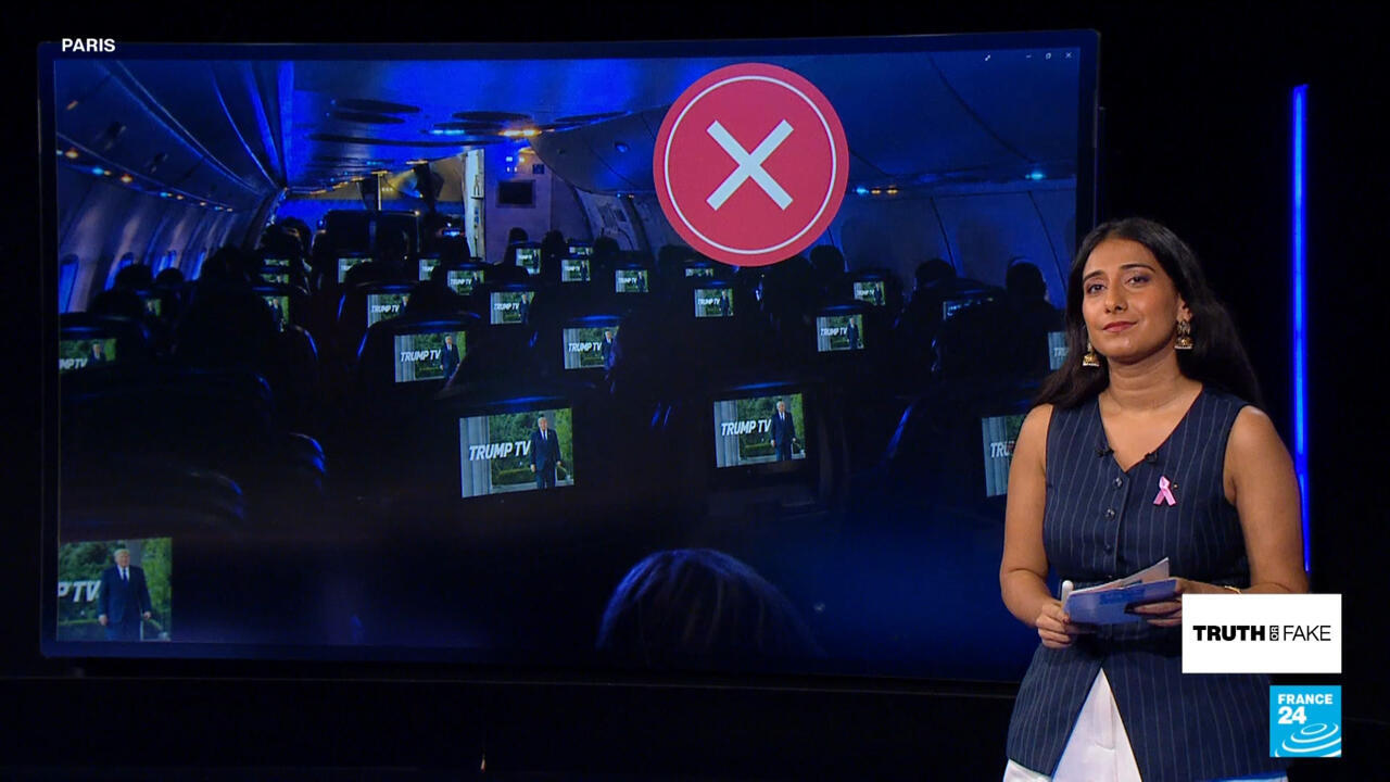 Presenter stands beside a large screen showing airplane seats with Trump TV monitors and a red X symbol.