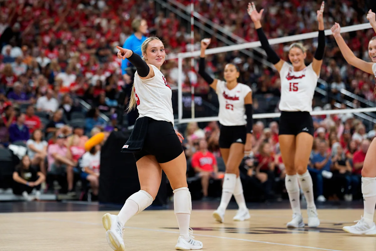 Nebraska volleyball players celebrate during a match as teammates raise their arms near the net.