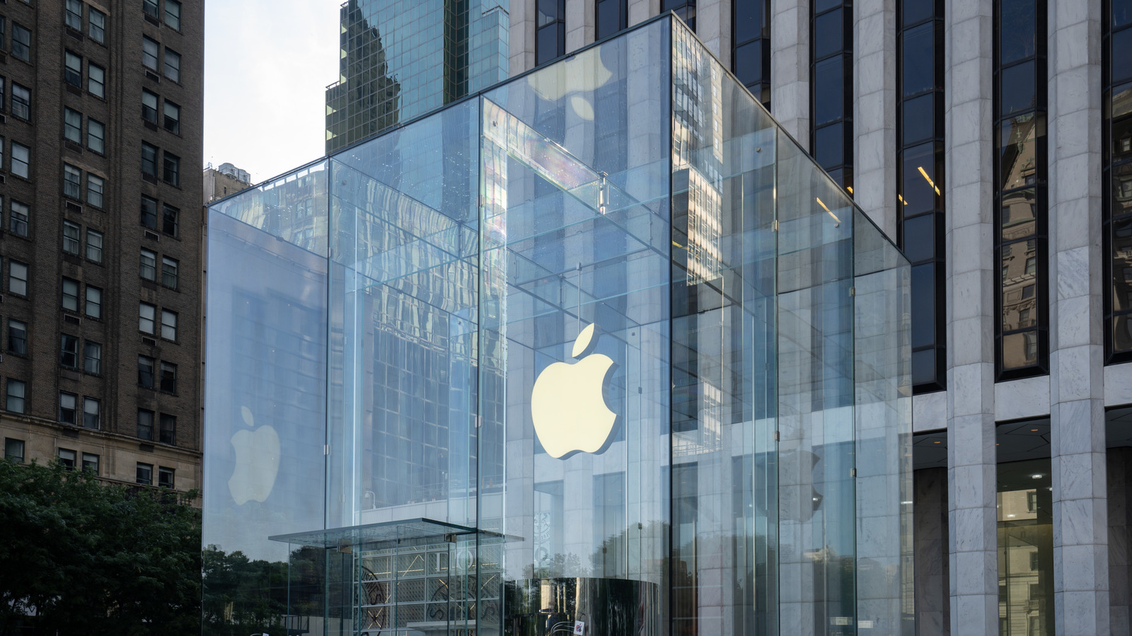 Glass-fronted Apple Store entrance reflecting surrounding city buildings and displaying a large Apple logo