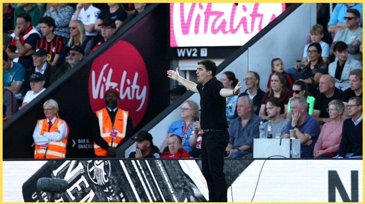 Football manager gesturing with arms out on touchline as spectators watch from stadium seats