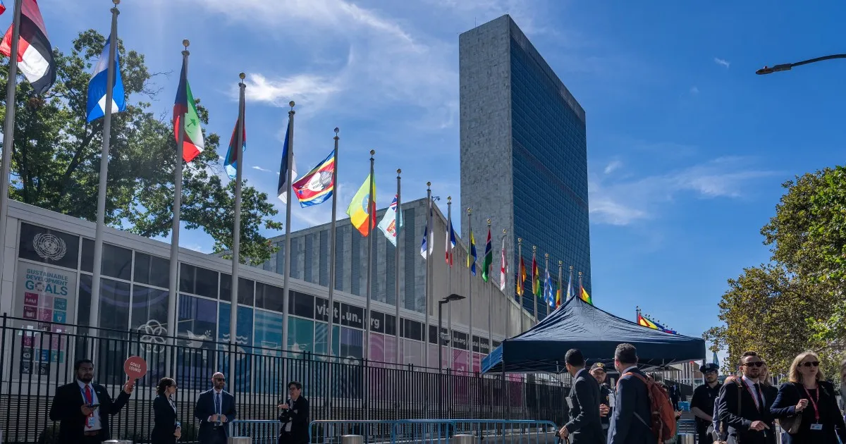 Flags outside a United Nations building under a clear blue sky with pedestrians in foreground