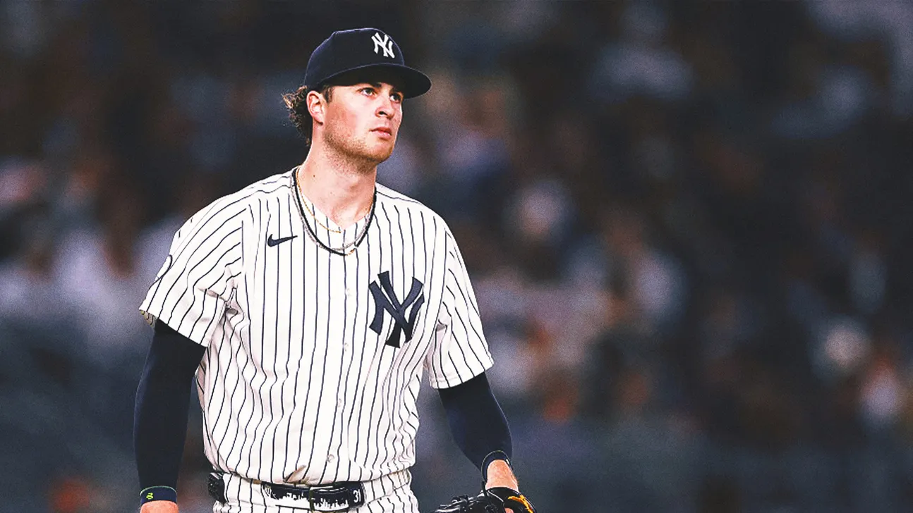 Yankees player in a pinstriped uniform and cap stands on the field against a blurred stadium crowd.