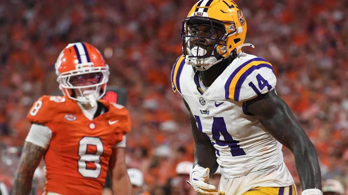 LSU football player in white uniform runs in foreground as Clemson player in orange follows