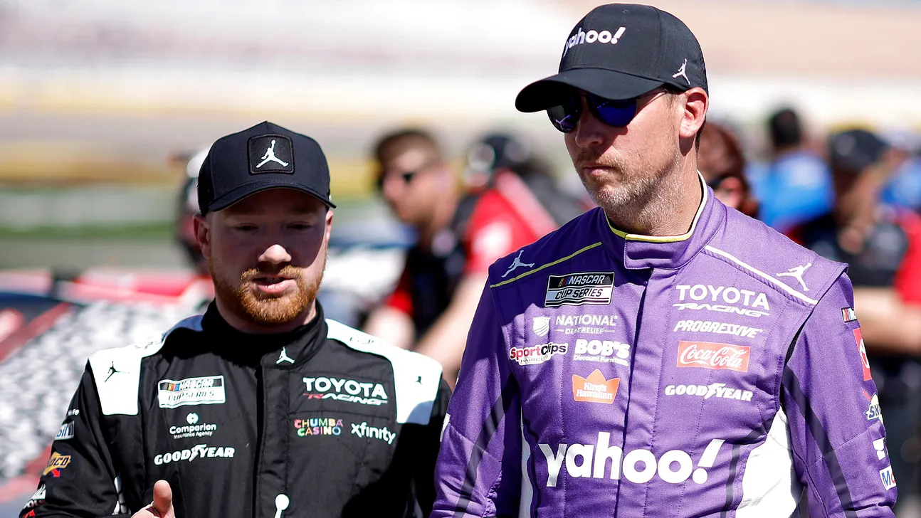 Two NASCAR drivers in Toyota Racing suits walk together at a racetrack.