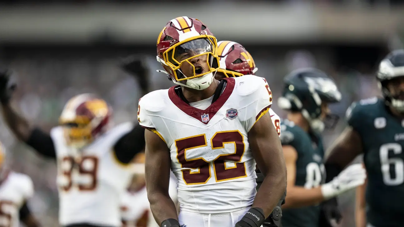 Football player wearing No. 52 in a Washington uniform stands on the field during a game.