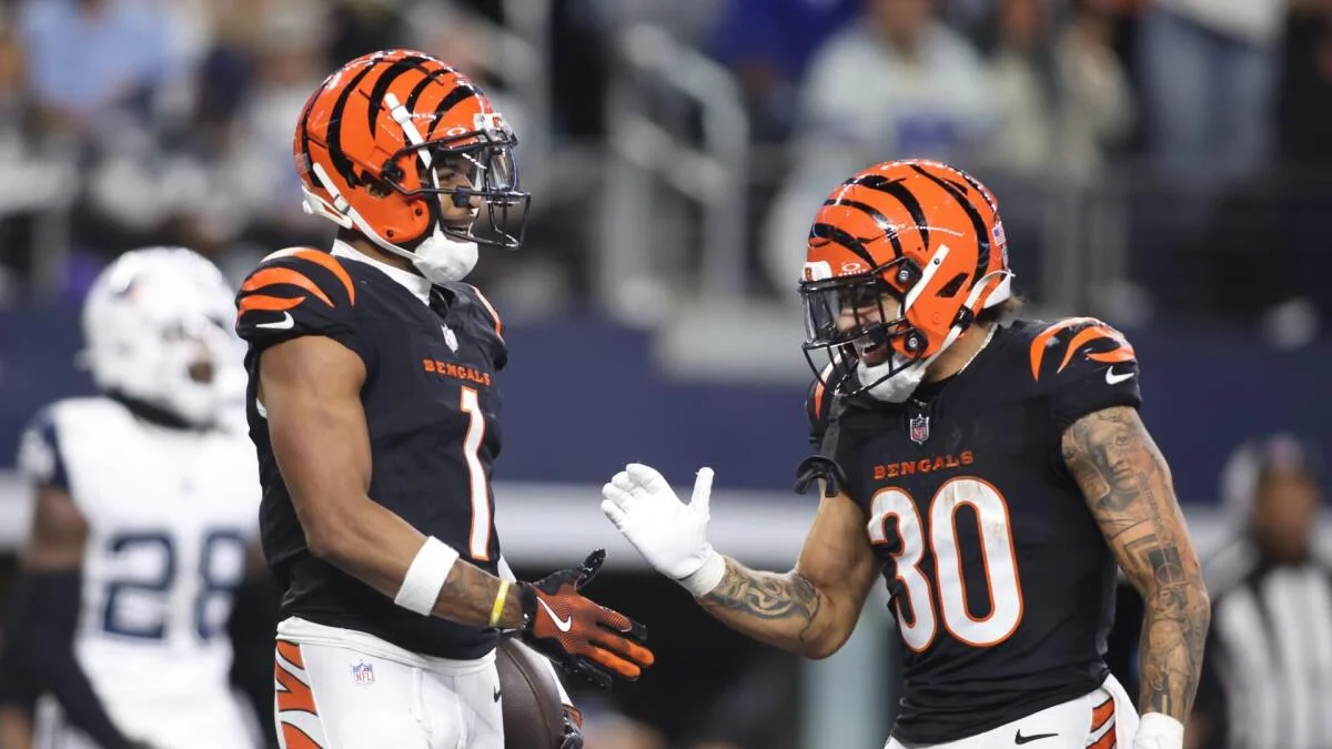 Two Cincinnati Bengals players in black uniforms and orange helmets gesture to each other during a game.