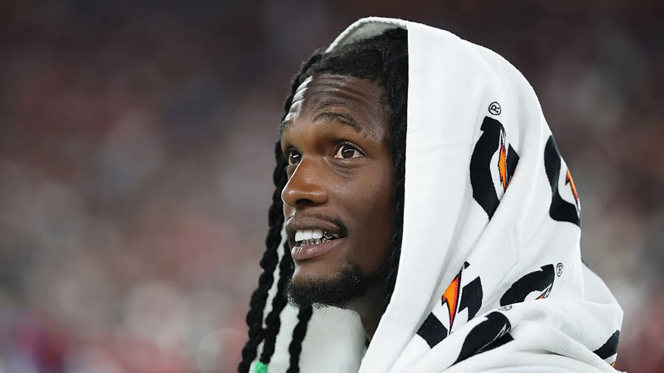 Football player with long dreadlocks wearing a white patterned hooded sweatshirt during a game