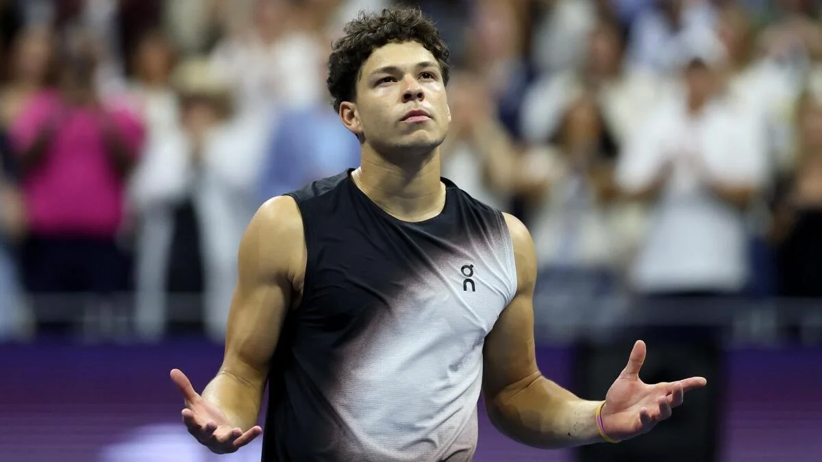 Tennis player in sleeveless shirt stands with arms outstretched before a blurred crowd