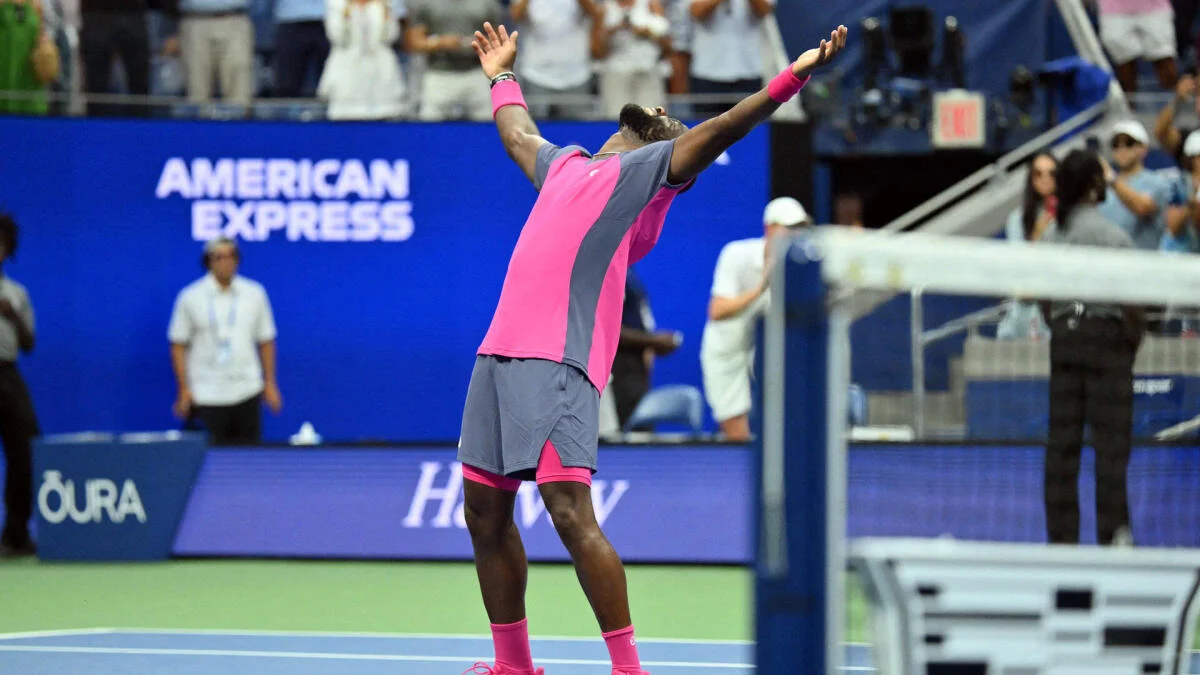 Tennis player in pink and gray raises both arms in celebration on court