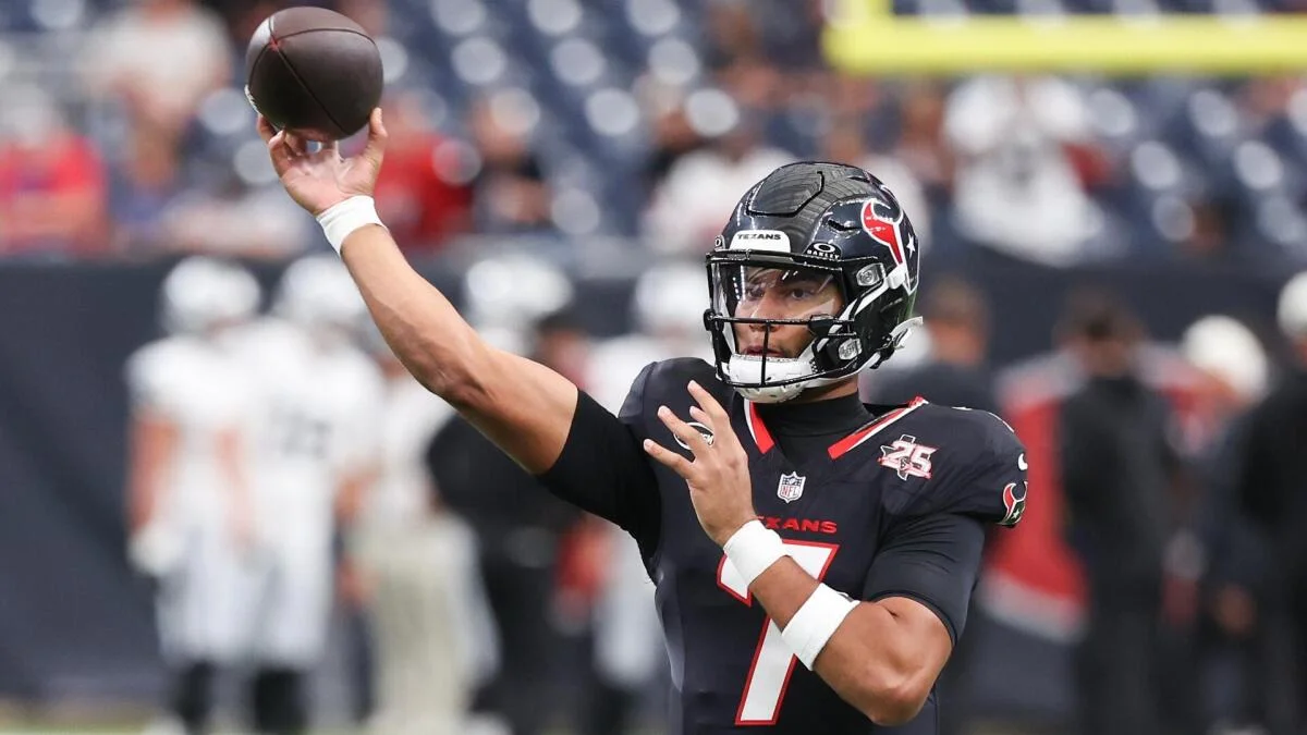 Football quarterback in a dark uniform throws a ball during a game.
