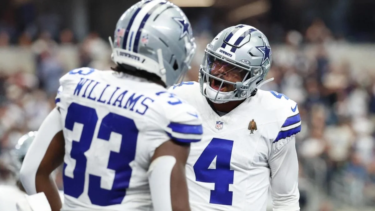 Two Dallas Cowboys players in white uniforms and silver helmets face each other on the field.