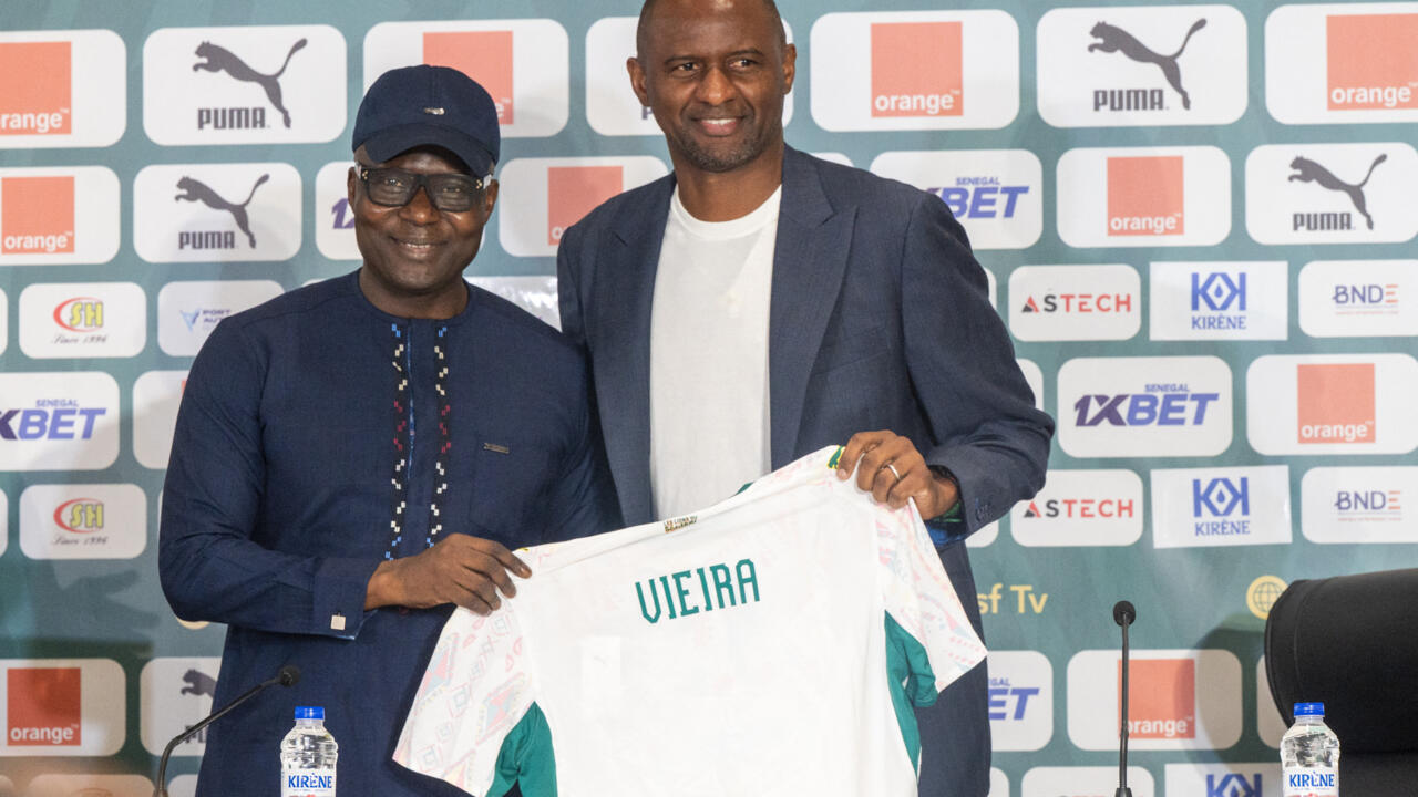 Two men pose together, holding up a white football shirt with “Vieira” printed on the back.