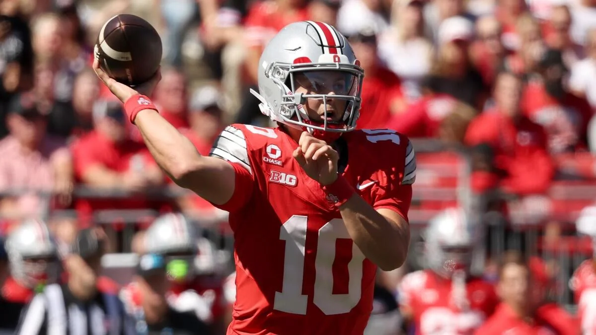 A quarterback in a red number 10 jersey raises a football to throw during a game.