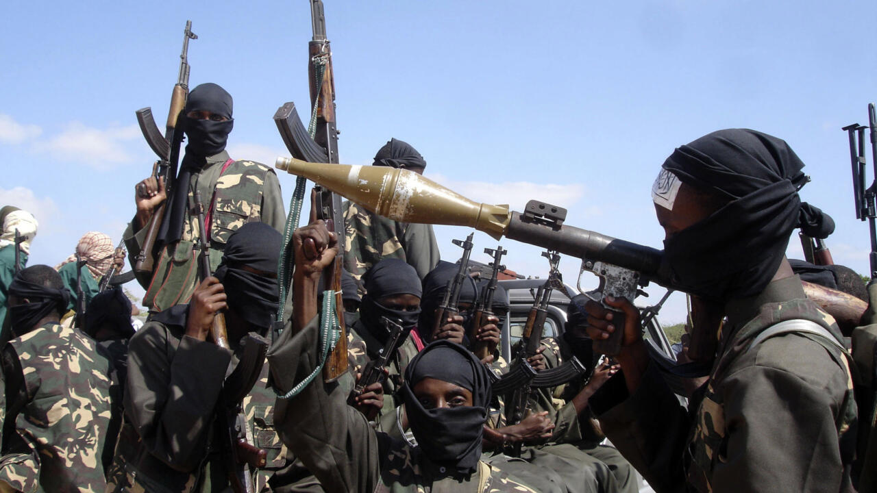 Masked armed fighters display rifles and a rocket-propelled grenade launcher outdoors under a clear sky.