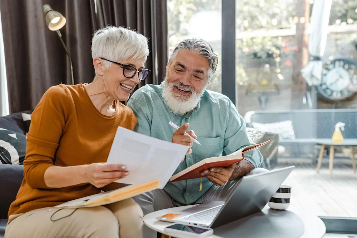 Older couple reviewing documents together beside an open laptop in a bright living room