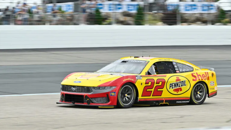 Yellow and red NASCAR race car number 22 speeds around a paved track.