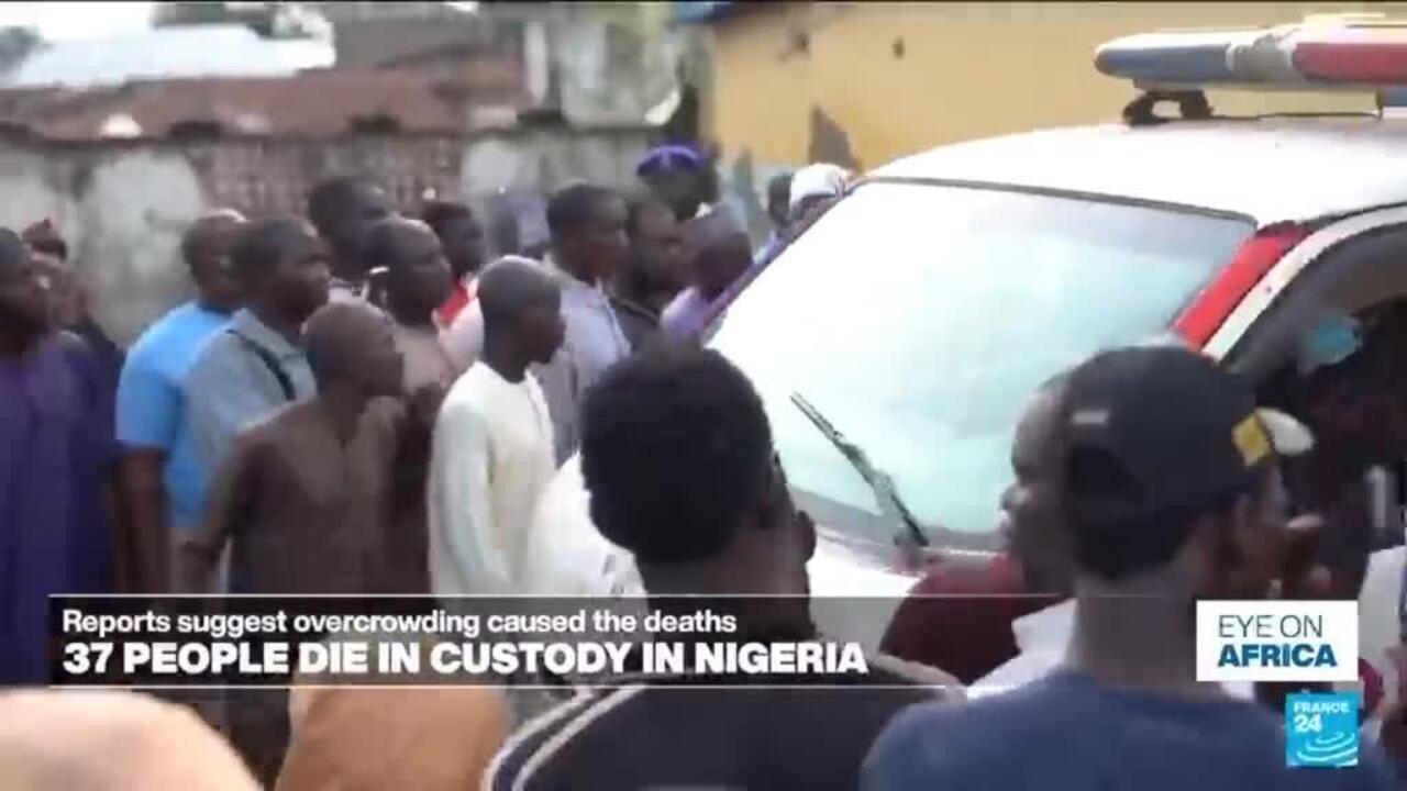 Crowd gathers around a police vehicle as officers appear to escort a person away.