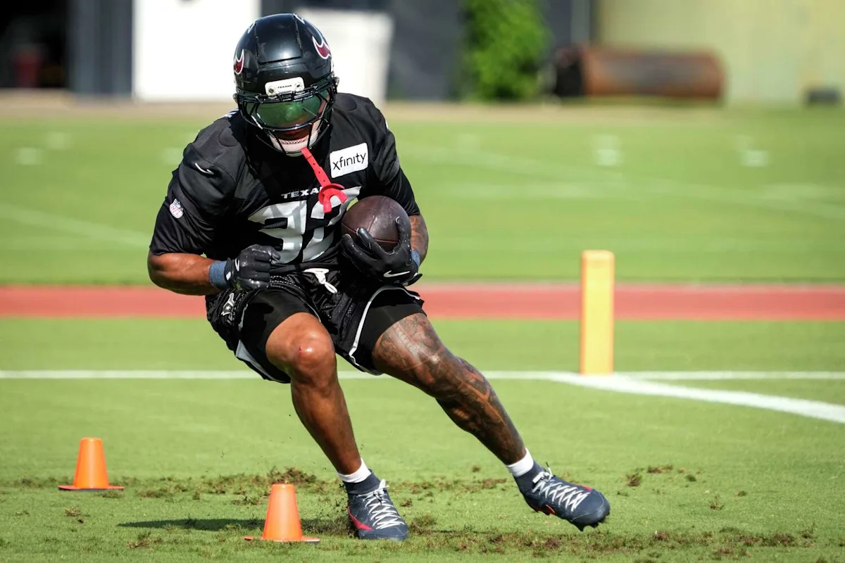 Houston Texans football player in helmet and pads runs with the ball during practice