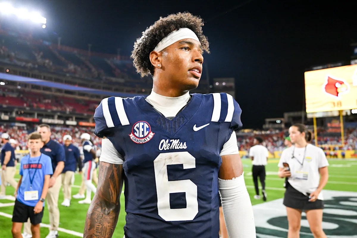 Football player wearing an Ole Miss uniform stands on the field during a nighttime game.