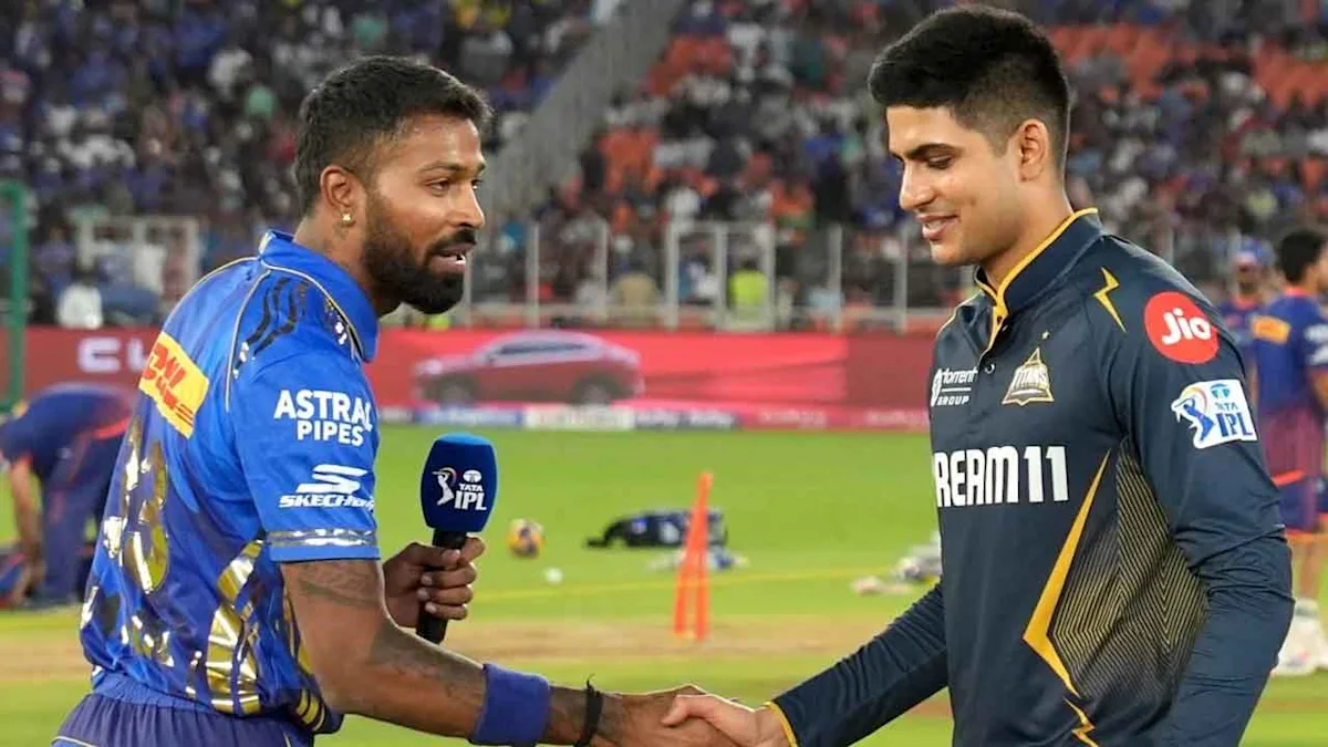 Two cricket players shake hands on the field, with one holding an IPL microphone.