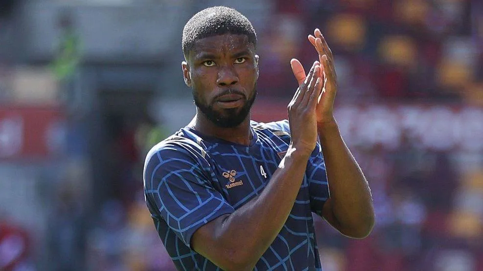 Footballer in a blue patterned jersey applauds with hands raised during a match