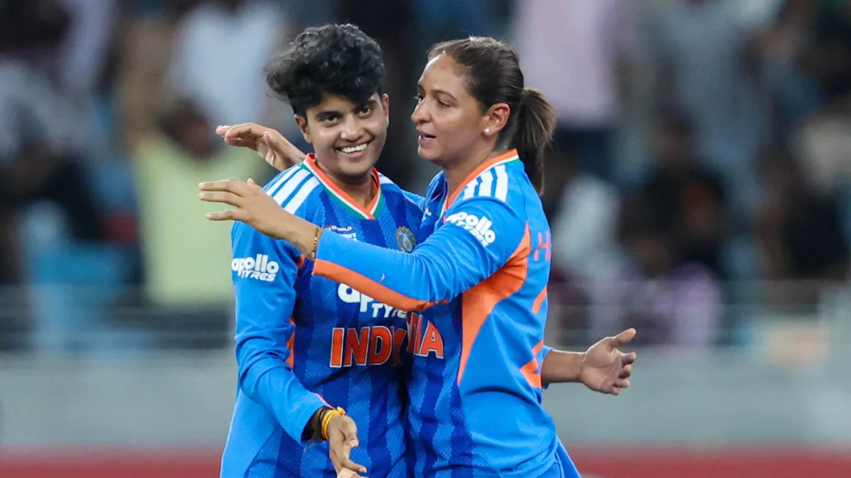 Two Indian women cricketers in blue jerseys embrace and celebrate on the field.
