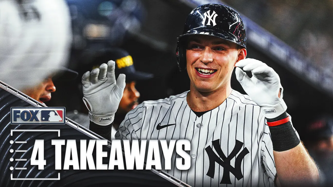 Smiling Yankees player raises both gloved hands while wearing a batting helmet and pinstriped uniform.