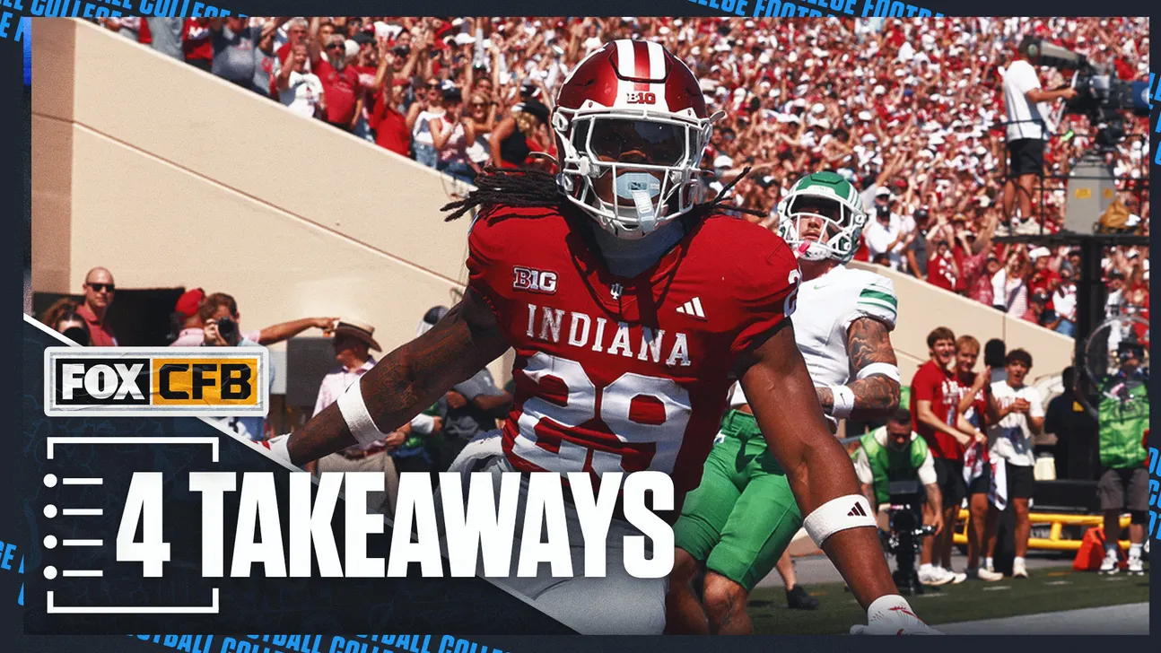 Indiana football player in red uniform runs past a North Texas player during a crowded stadium game.