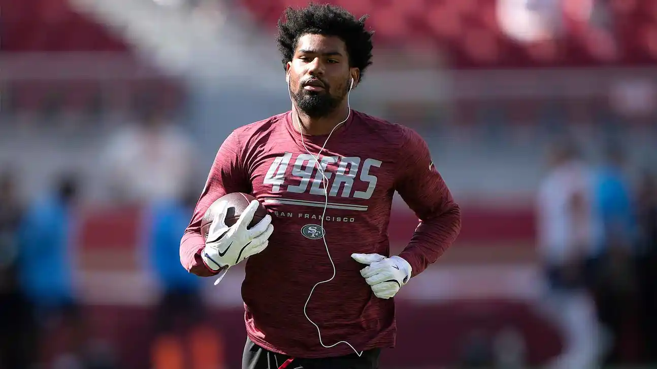 Football player in a 49ers shirt runs while carrying a football during practice.