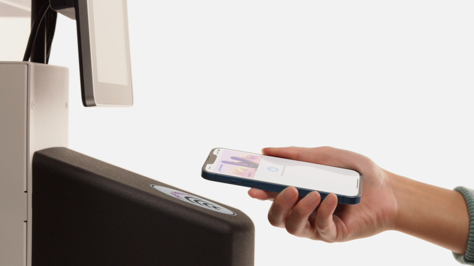 Person holds a smartphone near a contactless payment terminal bearing a wireless payment symbol