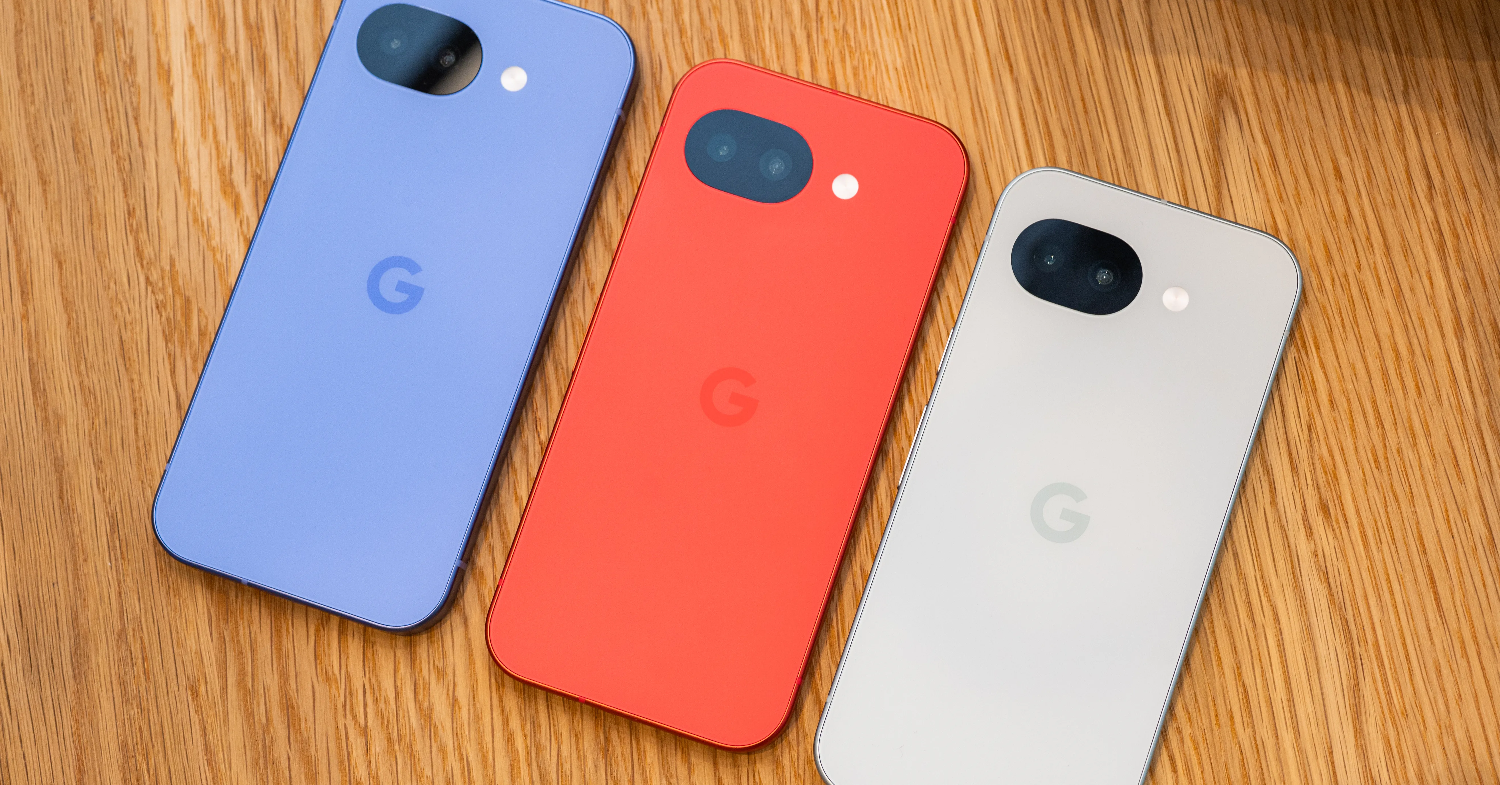 Three colorful smartphones with dual cameras and Google logos arranged on a wooden surface