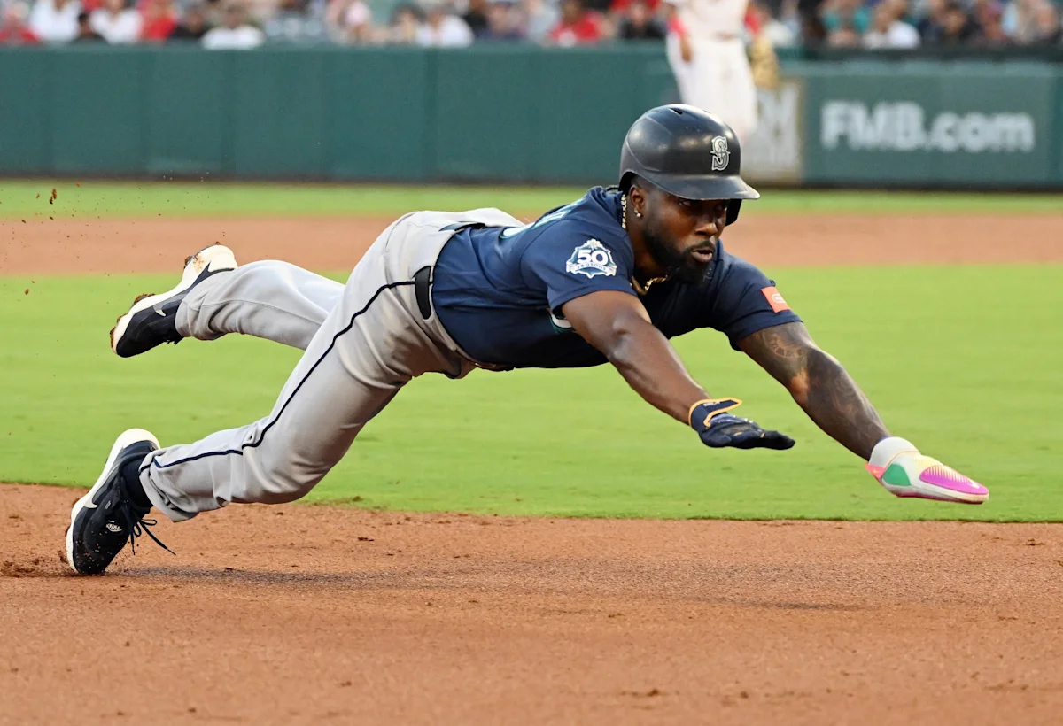 Baseball player dives horizontally across the infield while reaching toward a base during a game.