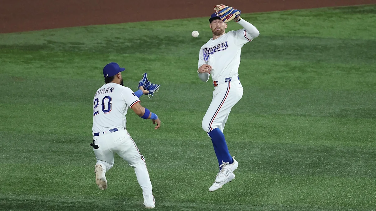 A Rangers pitcher delivers a pitch as a teammate watches from the field.
