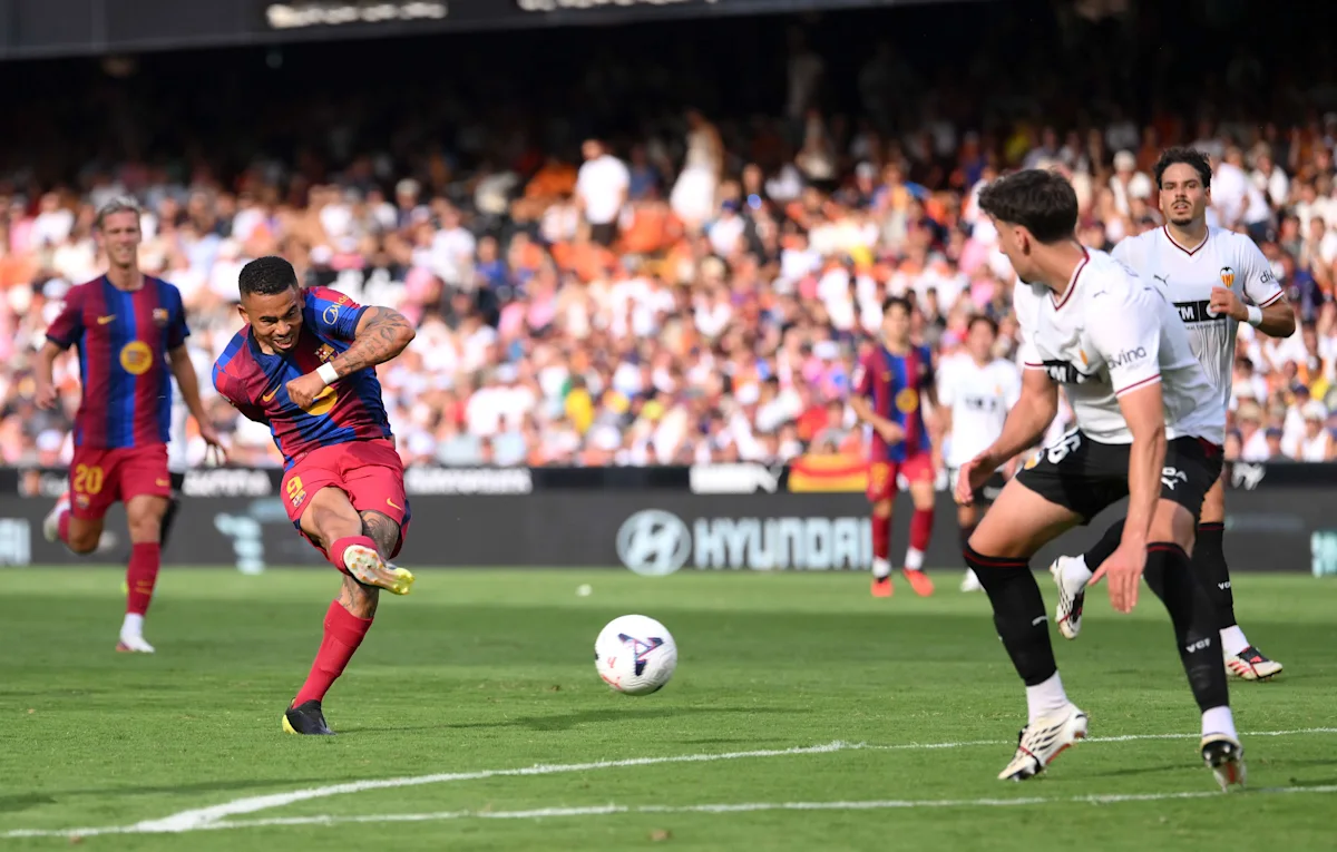 Barcelona player in red and blue strikes the ball as defenders in white and black close in.