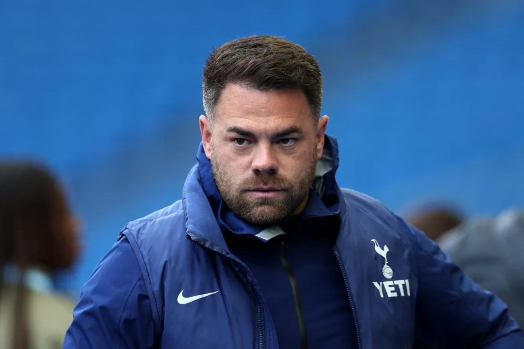 A man in a navy Tottenham Hotspur jacket stands against a blue stadium background.